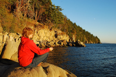 Woman meditating on a rock overlooking ocean.